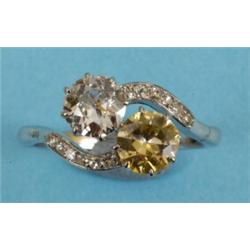 A Diamond Two Stone Crossover Ring, set one clear and one fancy yellow brilliant cut diamond, fla...