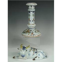 An 18th/19th century French faience figure of a seated cow and a candlestick, both painted wit...
