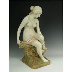 An early Royal Dux figurine of a semi clad female drying her feet and seated upon a rockwork base...