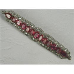 A ruby and diamond bar brooch set with two pearl shape and eleven emerald cut rubies surrounded b...