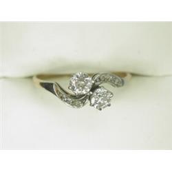 A 2-stone old cut diamond crossover ring with diamond set shoulders, set in white metal to a yell...
