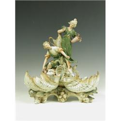 A 1920s Royal Dux style figure depicting two figures above shell shaped bowls, arms restored,...