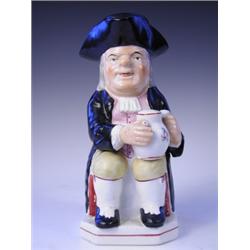 A Victorian Toby jug with a measuring cup in his triform hat, on a square base with canted cor...