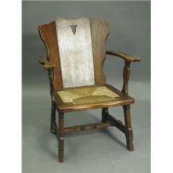 An oak Arts & Crafts style armchair having a three piece plank back with a pierced arrowhead m...