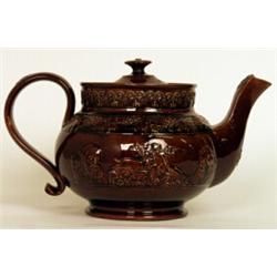 A large Staffordshire treacle glazed teapot and cover, mid 19th Century, decorated in relief with...