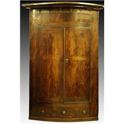 A George III mahogany and crossbanded bow front hanging corner cupboard, with twin hinged doors e...