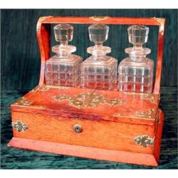 An Edwardian oak and brass mounted three bottle tantalus with twin hinged front compartments....