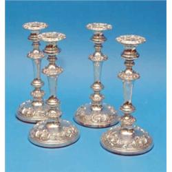 A set of four Victorian plated candlesticks, with scroll and shell banded stems and circular feet...