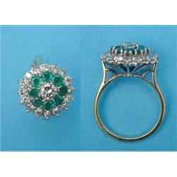 An 18ct gold circular cluster ring, central brilliant cut diamond bordered by a row of 8 emeralds...