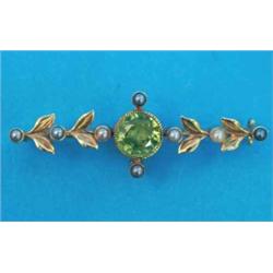 An Edwardian gold bar brooch, millegrain set with a round cut peridot flanked by pairs of leaves...