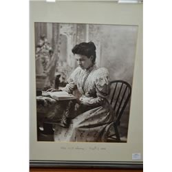 Black and white archived photo of a young woman reading at a table labelled "Mrs. W. J. Hewey - Sept