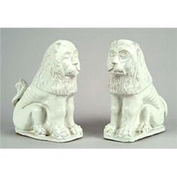 A pair of German fayence models of lions, seated on their haunches and painted with a white glaze...