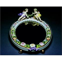A Figural Porcelain Mirror, German, 19th century, The ovular porcelain frame set with a dense fl...