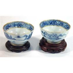 Pair of hand painted blue and white Chinese tea bowls on wooden stands, decorated with chinoiseri…