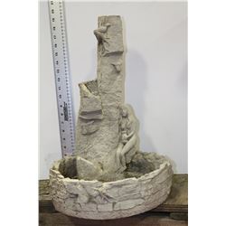 CONCRETE LADY SITTING BY WALL FOUNTAIN