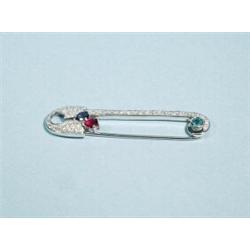 An 18 kt. white gold brooch in form of a safety pin. Set with diamonds , a facetted ruby, sapphir…
