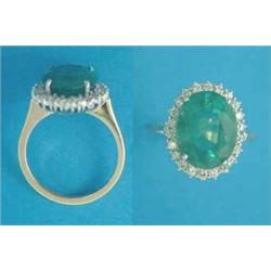 An 18ct gold cluster ring, claw-set with an oval emerald bordered by round cut diamonds...