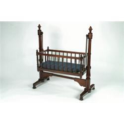 A MID-VICTORIAN MAHOGANY CRADLE, the rocking bassinet enclosed by turned spindles, hung from a tr...