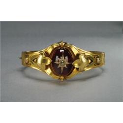 14K YELLOW GOLD HINGED BANGLE, with a central medallion bezel set with an oval garnet cabochon su...