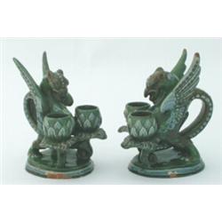 A pair of C H Brannam chambersticks, modelled as griffins, their tails fashioned as handles, on o...