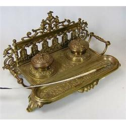 A late Victorian brass inkstand and quill pen, the latter rests in a trough before two inkwells and.