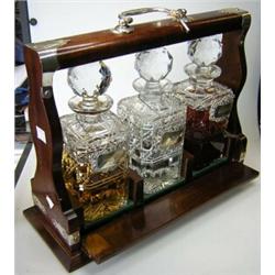A mahogany tantalus, together with three cut glass decanters and three silver labels for Whisky, Gi.