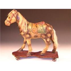A pull along papier mache horse, the dappled animal caparisoned with green saddle cloth, red and ye.