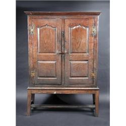 An 18th century oak cupboard on stand, the upper section with moulded cornice above a pair of arch p