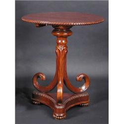 A mahogany tripod table, the circular top with carved edge supported on a scrolling column, standin.