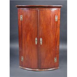 A George III mahogany bowfront hanging corner cupboard, the moulded cornice above a pair of doors e.