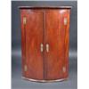 Image 1 : A George III mahogany bowfront hanging corner cupboard, the moulded cornice above a pair of doors e.