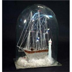 Victorian blown glass galleon with sailors climbing the ropes beside a lighthouse under a glass dome