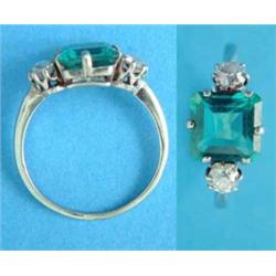 An emerald and diamond ring, the square cut emerald flanked by 2 round old brilliant cut diamonds...