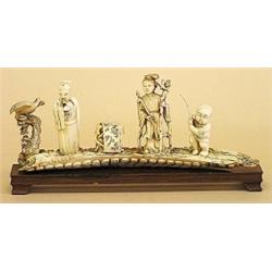 CARVED IVORY GROUP, Chinese. Of a man, a woman and a boy standing next to a table with an open...