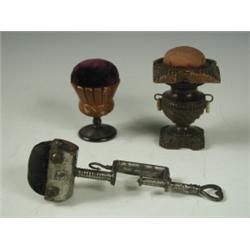 Three Victorian pin cushions: two in turned and carved wooden stands and one steel sewing clam...