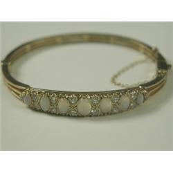 A 9ct gold hinged bangle set with 7 graduated oval opal cabochons and 14 round brilliant diamo...