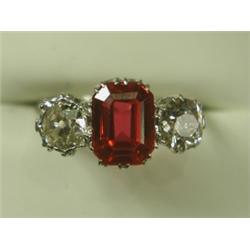A three stone ring set with a central trap cut synthetic ruby and two old cut diamonds in plat...