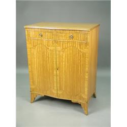 A satinwood serpentine front cupboard, with inlaid banding, the interior with a glass shelf an...