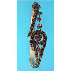A 9ct. gold tubular hinged bangle, the front with a garnet and seed pearl set heart and star moti...