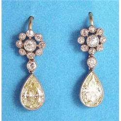 A pair of diamond pendant earrings each with a millegrain set pear shape fancy yellow diamond dro...
