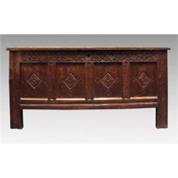 An early 18th Century oak coffer, the quadruple panelled hinged top over a rosette and foliate ca...