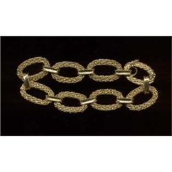 An 18ct gold bracelet, c.1985, each oval link of entwined design and joined by a single plain con...