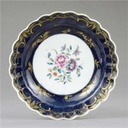 A Worcester deep plate, painted with central flower sprays, the wide royal blue border gilt with...
