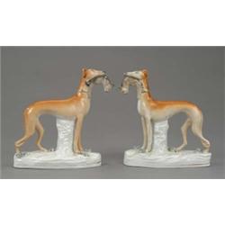 A pair of Staffordshire figures of standing greyhounds, with shaded tan coats and each holding a...