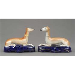 A pair of Staffordshire figures of resting greyhounds, with shaded tan coats and detailed muzzles...
