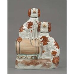 A Staffordshire group of two seated spaniels, with brown splashed coats, one seated on a barrel,...