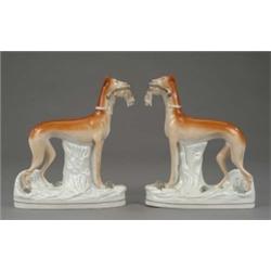 A pair of Staffordshire figures of standing greyhounds, with shaded tan coats, each with a hare i...