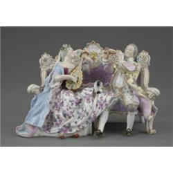 A Meissen group of two musicians, seated on a sofa, he with flute and wearing yellow ground flora...