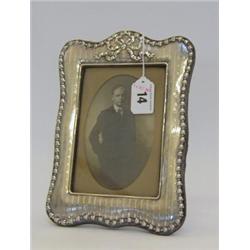 A SILVER EASEL PHOTOGRAPH FRAME, bow and ribbon border, machine engraving, rectangular opening 13...