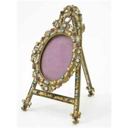 A late 19th century gilt metal and enamel miniature frame, in the form of an oval frame on an eas...